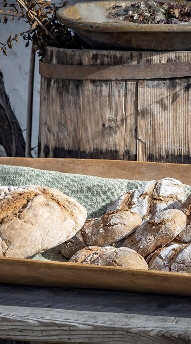 Floured loaves and small bread rolls in a wooden trough in front of an old wooden barrel. | © Lichtfarben