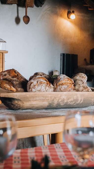 Loaves in a wooden bowl beside the oven during bread baking at Dietlgut in Hohe Tauern National Park. | © Monja Kraner