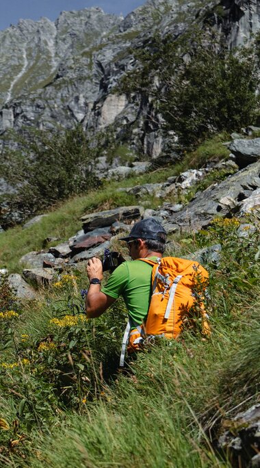 Hiker with a backpack photographs a rocky mountainside in the Sulzbachtäler Wilderness Area. | © Nationalpark Hohe Tauern, Kathrin Egger