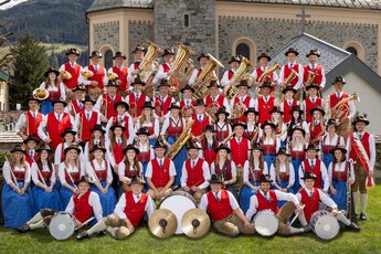 Trachtenmusikkapelle Niedernsill beim Gruppenfoto in Tracht mit Blas- und Schlaginstrumenten vor einer Kirche. | © TMK Niedernsill, Foto Nici Faistauer