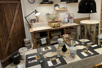 Kreativraum mit gedecktem Arbeitstisch, Pinseln, Farben, Keramikformen, Regalen und einem Brennofen. | © Keramik Boutique - Jessica Ritsch 