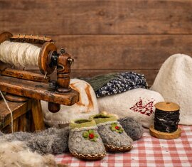 Schafwolle, Spinngerät, Garn sowie gefilzte und gestrickte Handarbeiten auf einem Tisch. | © KI generiertes Bild